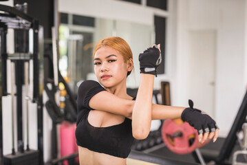 A young woman in a black crop top does a shoulder stretch before a workout session at the gym. Warming up upper body properly.
