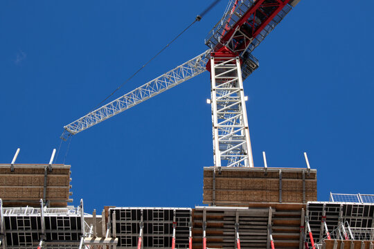 A construction crane is seen on a clear sky day, while on-site building a condo, apartment building.  