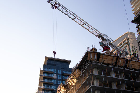 A closeup of a crane construction at work on a clear day. In operation, lifting a piece for a construction site building a condo.