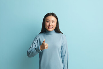 Smiling Woman Showing Big Fingers Isolated. Asian Girl Looking at Camera with Toothy Smile and Showing Thumb Up, Approval Sign, Satisfied with Service, Good Feedback. Indoor Shot on Blue Background 