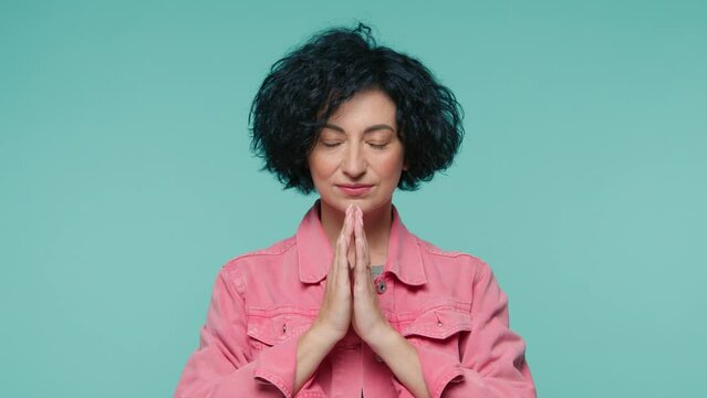 Face portrait of calm mature beauty woman hands gently folded in namaste gesture symbol of salutation and spirituality recognition of the unity and eternal spirituality, slow motion studio 4K footage