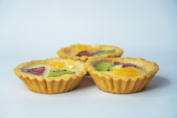 A small plate of a typical Indonesian snack called Pie Susu topped with slices of orange, strawberry and kiwi, served on a white background