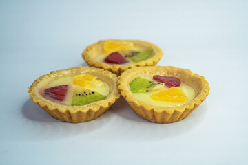 A small plate of a typical Indonesian snack called Pie Susu topped with slices of orange, strawberry and kiwi, served on a white background