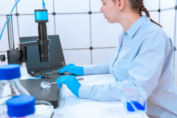 young woman laboratory assistant examines a sample of a geological mineral under a microscope in a...