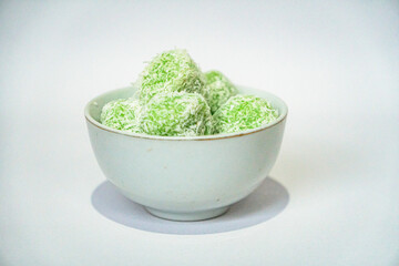 A traditional Indonesian snack called klepon, made from green glutinous rice and inside there is brown sugar, small round shape with grated coconut topping, served in a small bowl on a white backgroud