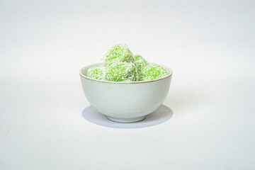 A traditional Indonesian snack called klepon, made from green glutinous rice and inside there is brown sugar, small round shape with grated coconut topping, served in a small bowl on a white backgroud
