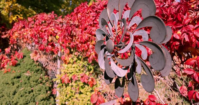 Twirling yard decoration spins in the breeze against bright red fall leaves