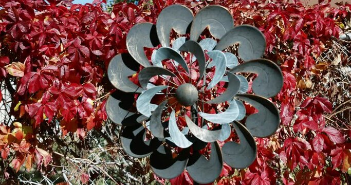 Twirling yard decoration spins hypnotically against background of red fall leaves leaving on mesmerized by the motion and color.