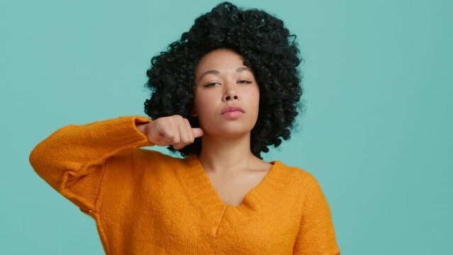 Calm angry African American lady show sign cut hand neck isolated blue background. Adult female looking at camera threatening cutting throat with hand show killing gesture of revenge aggression studio