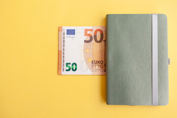 Fifty euro banknotes next to a notebook on a yellow background, Expense and budget planning. Cash paper currency, payment, earnings and savings, the concept of money and finance