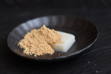 Mochi sprinkled with soy flour on black plate under black design board. Flour rice cake.