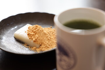 Mochi sprinkled with soy flour with Japanese green tea on black plate under black design board. Flour rice cake.