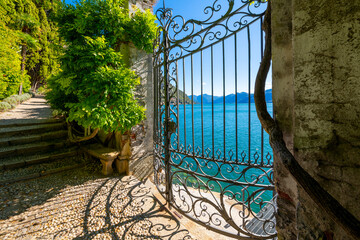View from a lush walking path and garden with wrought iron gate of the mountains and Lake Como from...