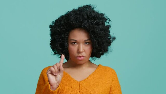 No gesture by African American woman with curly hair. Bad idea. Wrong choice. Refusal disagreement. Negative advice. Dissatisfied skeptic woman warning with finger wag in studio background slow motion