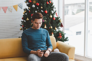 A single man seems lonely using his phone in his living room decorated with Christmas trees