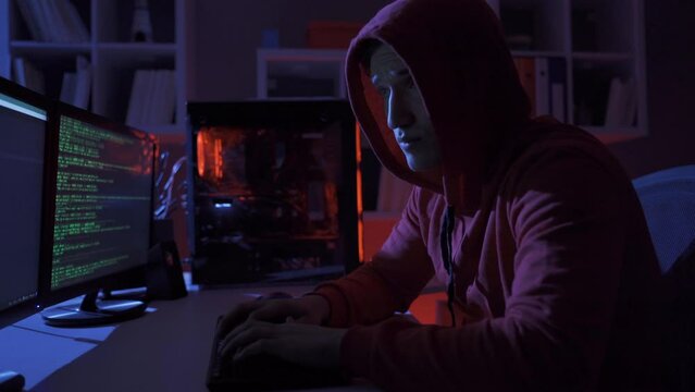 Male hacker using computer to commit a crime.
Hacker sitting near computer monitors with green code screens.
