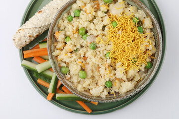 An Indian meal called upma, like a thick porriage made from roasted semolina or rava served with papad in a bowl on a green plate on a white background 