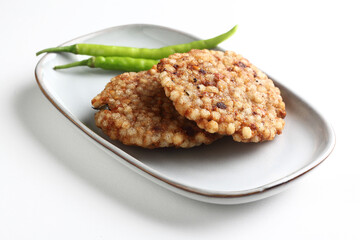 A crisp fried India snack called Sabudana Vada made from tapioca seeds, roasted peanuts, boiled potato and herbs served in white plate placed on a white background 