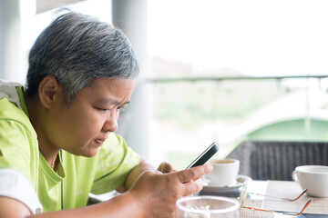 Asian senior businesswoman working at cafe using smartphone device, playing social media for looking posts chatting to friends. Browsing social networks for entertainment, sharing reunion enjoying