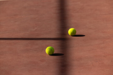 Tennis ball on clay court two separated by shadow