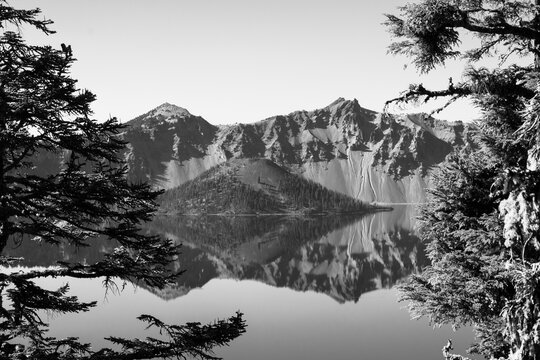 Black and white image of the Wizard Tower in Crater Lake, Oregon.  The crystal clear water creates a mirror reflection of the island and the surrounding crater wall. 