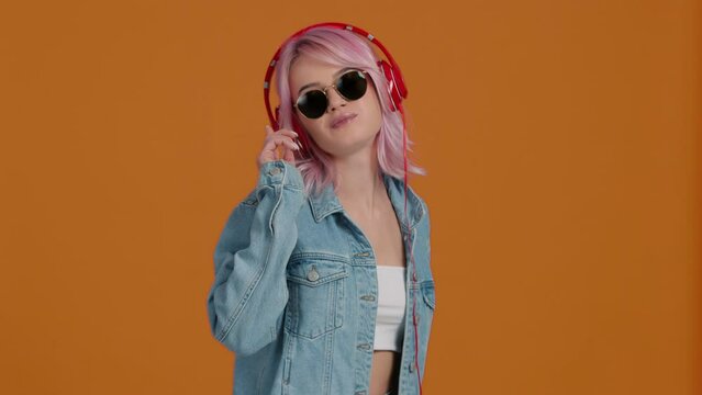 Young hipster girl feeling cool in sunglasses and wireless headphones dancing while chewing gum. Cheerful stylish blonde girl in hat and sunglasses dancing and smiling on isolated background 4K