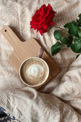 Top view of the morning breakfast in bed with cappuccino coffee on a tray and a red rose flower. Holiday greeting card