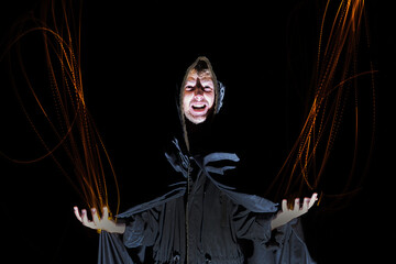 a sorcerer in a black cloak throws fire from his hands on a black background Halloween concept