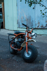 A motorcycle parked on a side road behind a wood building.  THe bike is orange 