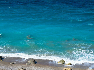 Obraz premium Beautiful and deserted beach on the west coast of Rhodes near Kamiros. Turquoise sea water, blue cloudless sky, pebble beach. Tourism and vacations concept. Space for text.