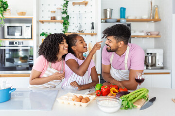 Happy loving family are preparing bakery together. Mother, father and child daughter girl are cooking cookies and having fun in the kitchen. Homemade food and little helper.