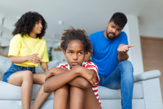 Family Misunderstanding, Childhood Problems. Sad offended black daughter sitting on the floor, turning back to parents after quarrel at home, upset mom and dad asking resentful girl what's wrong