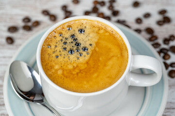 White porcelain cup with a freshly brewed espresso coffee and coffee beans on the table.