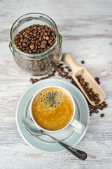 Freshly brewed coffee mug and glass jar with roasted coffee beans on a vintage table.