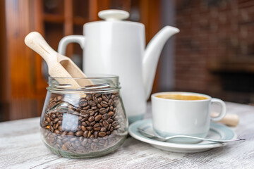 Coffee set with cup of freshly brewed coffee, porcelain coffee maker and glass jar with coffee beans.