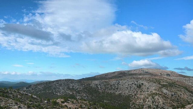 Pan shot footage shows a  a mountain's ridge with clouds moving fast in the blue sky.