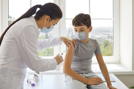 Female doctor makes antiviral vaccine injection for preteen boy in vaccination center. Child in protective mask receives booster dose of covid-19 vaccine. Concept of vaccination of children.