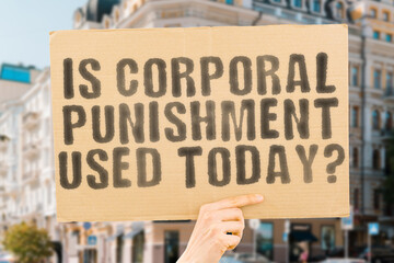 The question " Is corporal punishment used today? " is on a banner in men's hands with blurred background. Hit. Measure. Method. Parent. Teaching. Violent. Stop. Social. Teen. Beating. Aggression