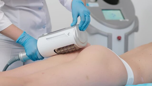 The masseur makes an hardware massage on the patient's legs in a white suit, close-up in a beauty salon.