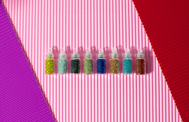 A lot of round jars with colorful bright sequins lie on a pastel pink background. Sparkling sequins. View from above. Shiny products in transparent bottles, close-up