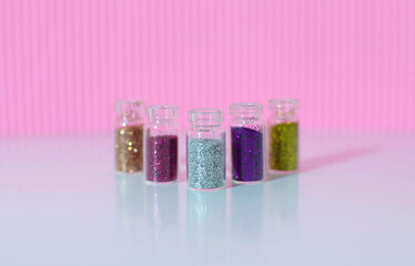 Lots of round jars with colorful bright sequins on a pink background. Sparkling sequins. Shiny products in transparent bottles, close-up. Selective focus