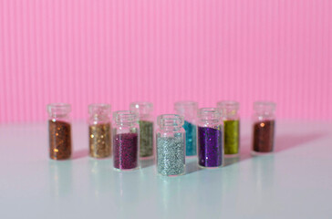 Lots of round jars with colorful bright sequins on a pink background. Sparkling sequins. Shiny products in transparent bottles, close-up. Selective focus