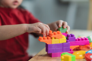 Asian cute funny preschooler little girl in a colorful shirt playing with blocks or construction toy blocks building a tower in kindergarten room or living room. Kids playing. Children at day care.
