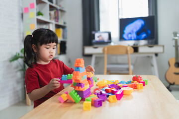 Asian cute funny preschooler little girl in a colorful shirt playing with blocks or construction...