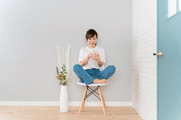 Fototapeta na wymiar 家で椅子に座りながら笑顔でスマホを使うアジア人女性 