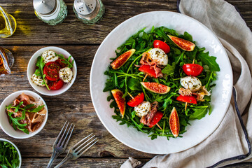 Fresh salad - mozzarella, crudo ham, fig, cherry tomatoes and leafy greens on wooden table
