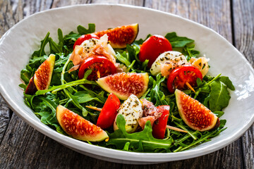 Fresh salad - mozzarella, crudo ham, fig, cherry tomatoes and leafy greens on wooden table
