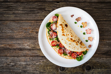 Italian piada wraps - piadina stuffed with fresh vegetable leaves, parmesan and prosciutto crudo on wooden table
