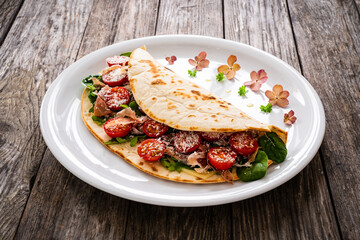 Italian piada wraps - piadina stuffed with fresh vegetable leaves, parmesan and prosciutto crudo on wooden table
