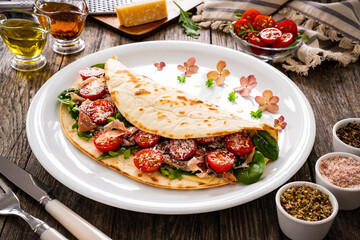 Italian piada wraps - piadina stuffed with fresh vegetable leaves, parmesan and prosciutto crudo on wooden table
